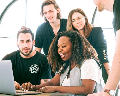 A diverse group of young professionals collaborating around a laptop in a modern office setting. Perfect for business or tech concepts.