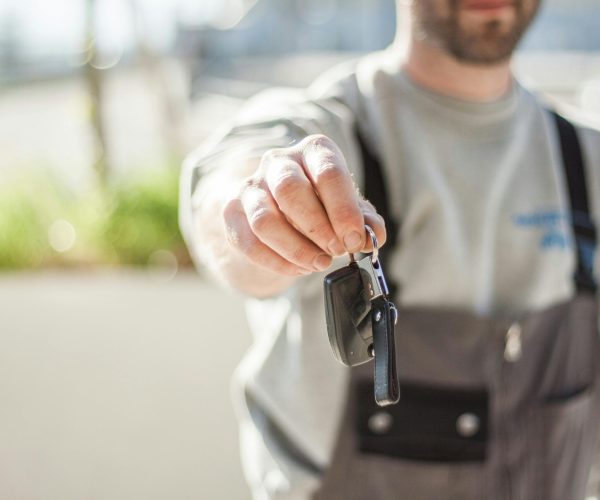 Hand holding a car key outdoors, blurred background, shallow focus.